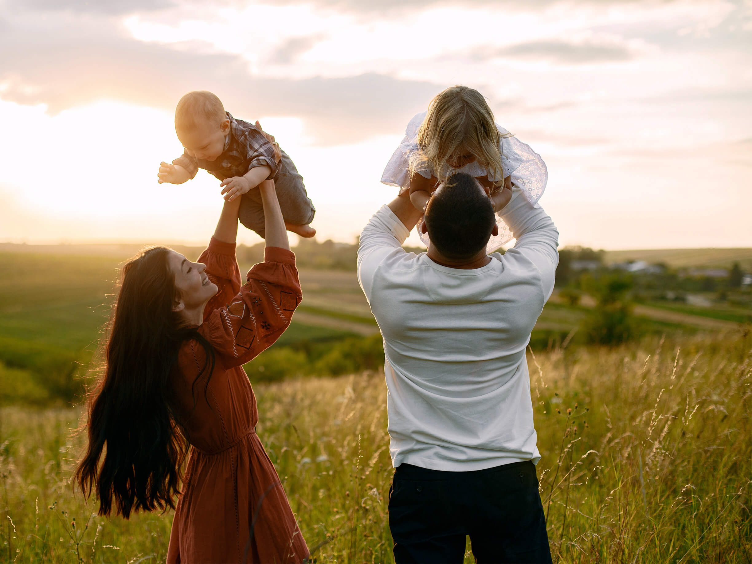 A man and a woman each holding children over their heads in a field.