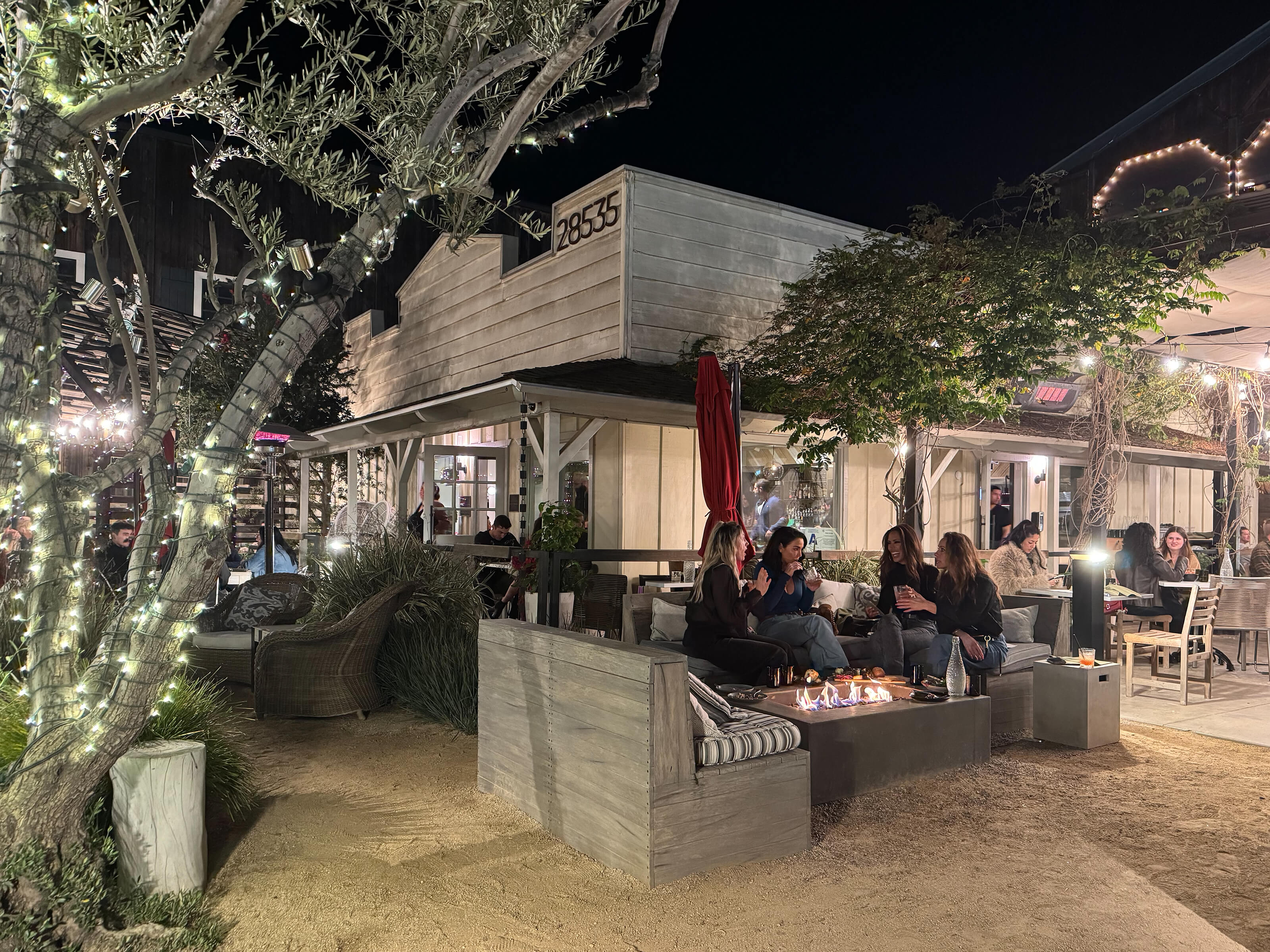 Guests with drinks sitting around an outdoor fire table.