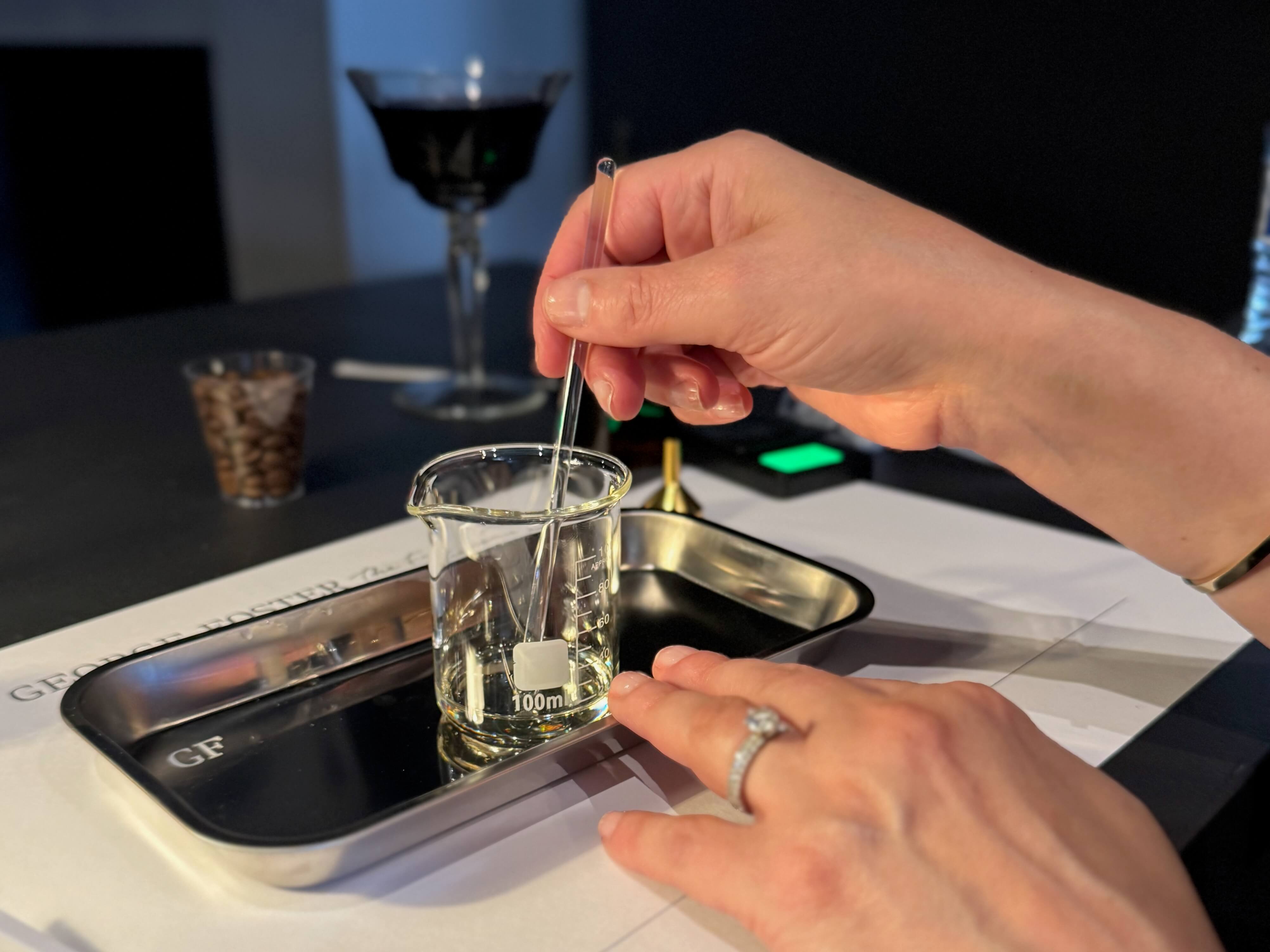 A hand stirring liquid in a very small beaker.
